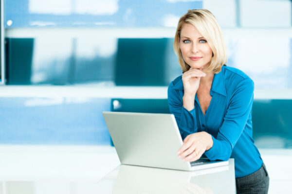 Blond Businesswoman in Modern Office with Laptop Computer Attractive young woman uses a computer to develop effective prospecting messages