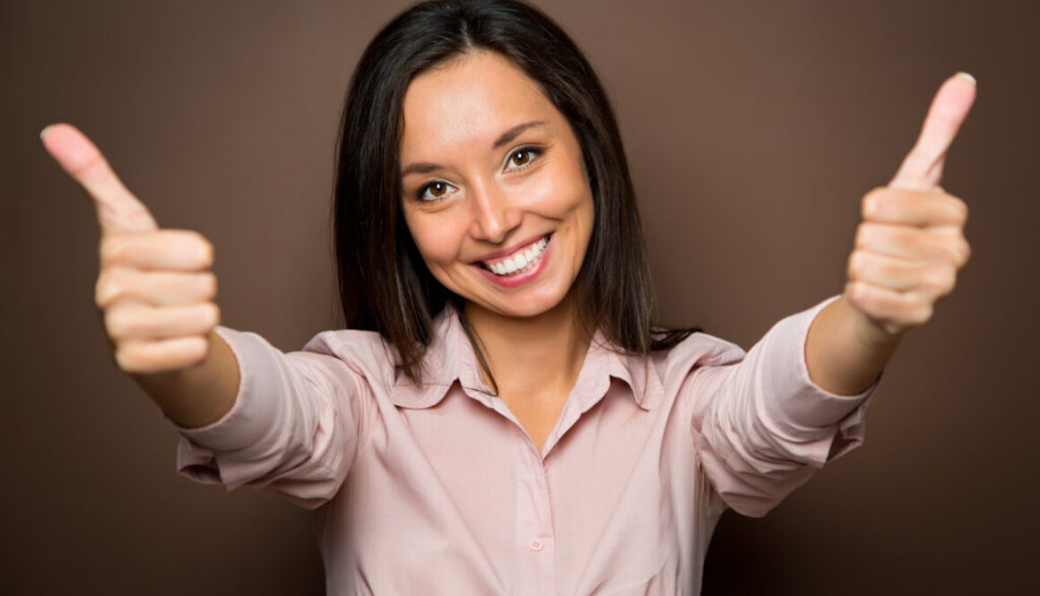 Cheerful young brunette woman gives two thumbs up