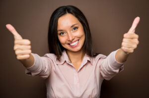 Cheerful young brunette woman gives two thumbs up