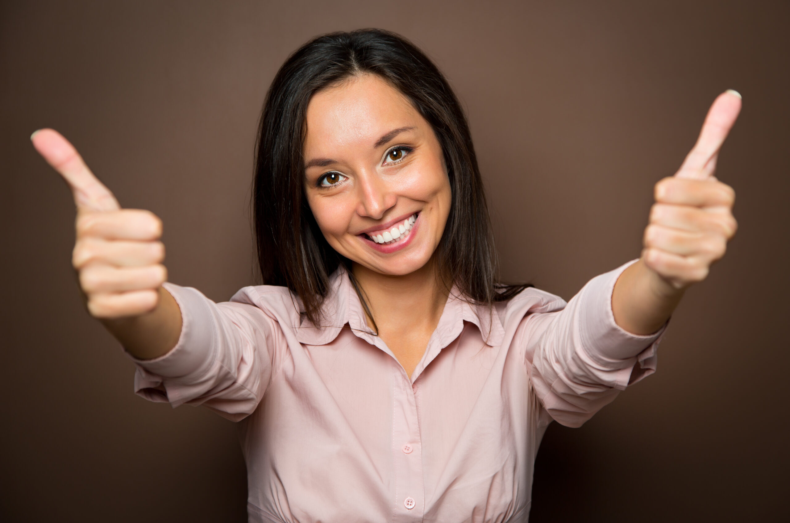 Woman giving thumbs up approval hand sign gesture smiling happy Cheerful young brunette woman gives two thumbs up