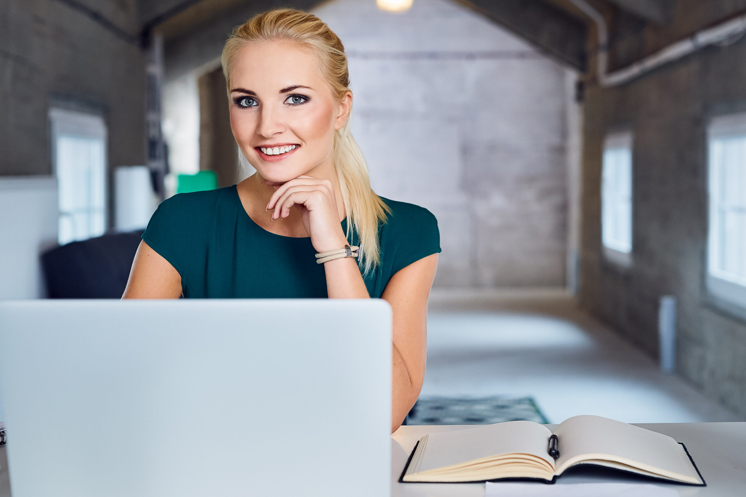 cheerful businesswoman sitting at the table in modern office, looking at camera