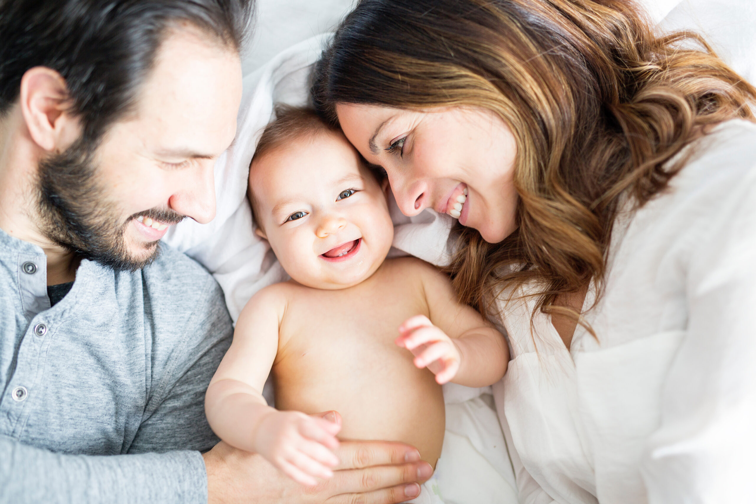 Mother father and baby child on a white bed. Young happy couple with baby