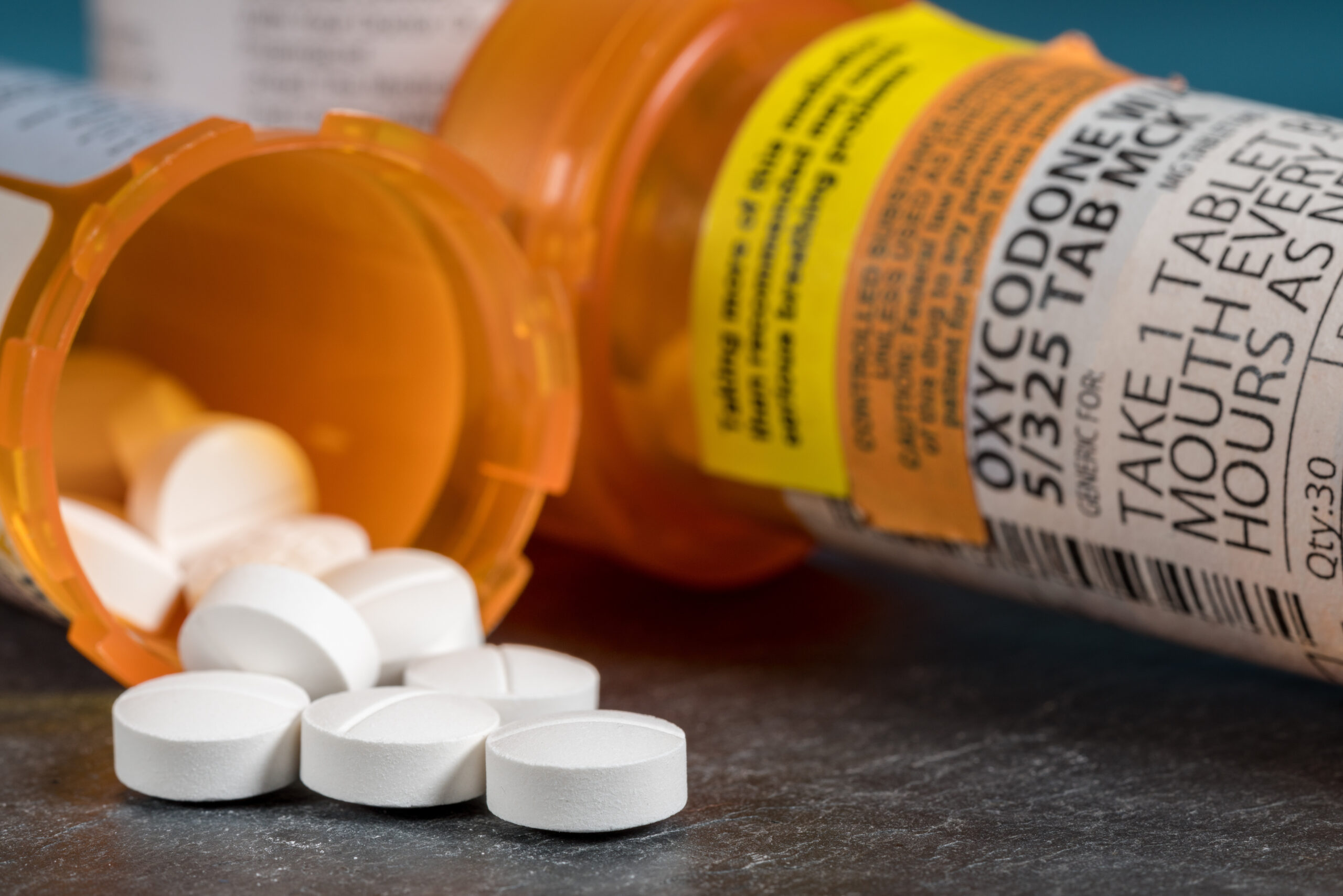 Macro of oxycodone opioid tablet bottle Oxycodone narcotic pills spilling out of an open pill container; the image will be used for a post discussing life insurance exclusion riders