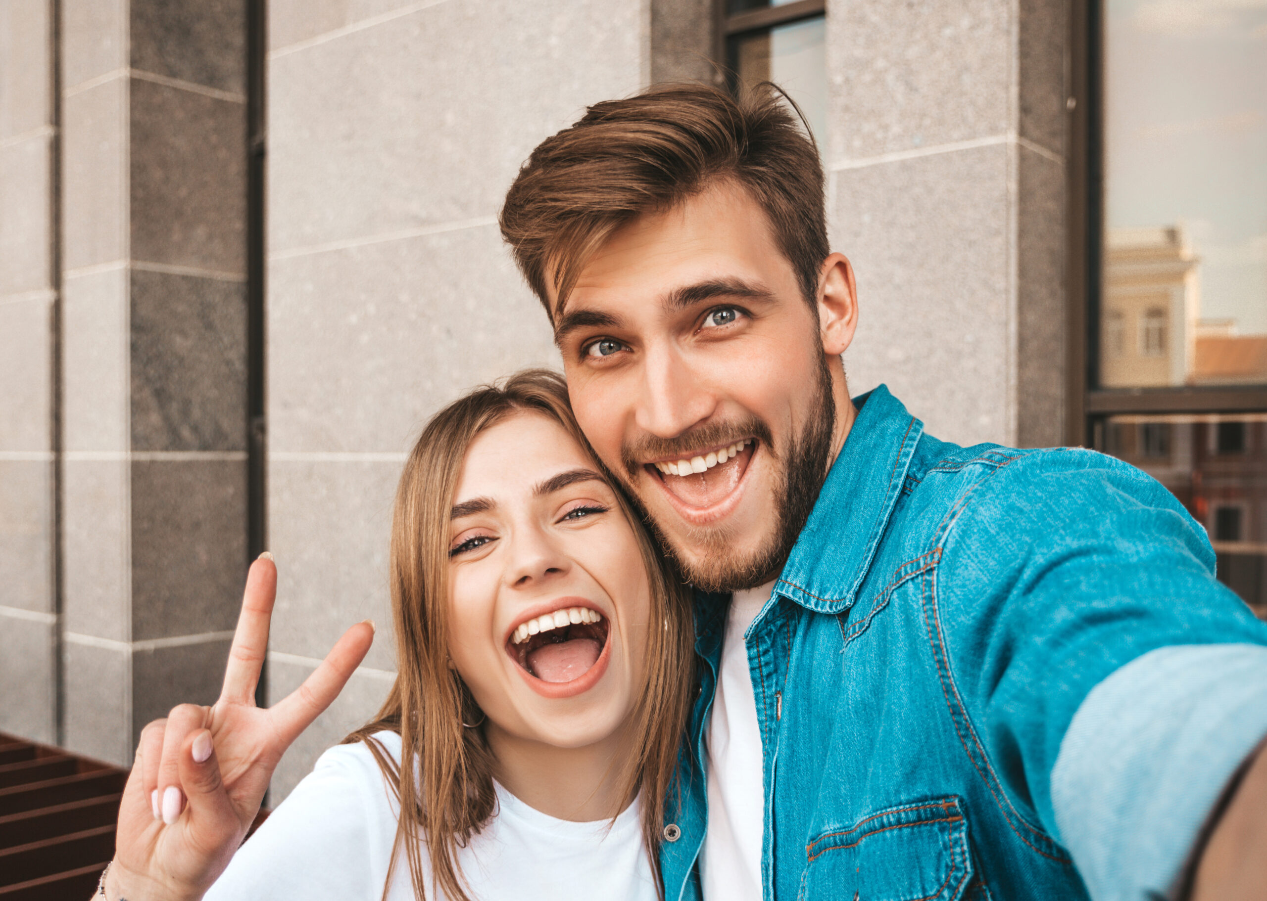 Smiling beautiful girl and her handsome boyfriend in casual summer clothes. Happy family taking selfie self portrait of themselves on smartphone camera. Having fun on the street background