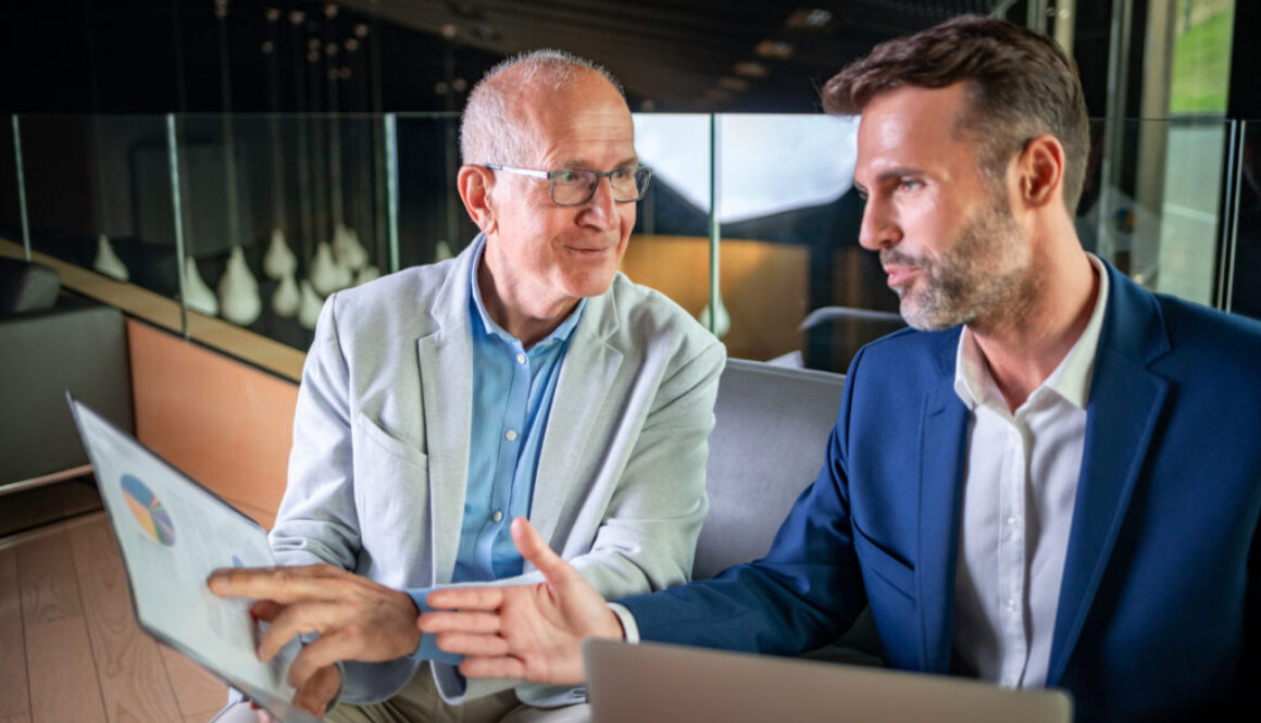 Younger and older businessman talking about documents during meeting in modern business lounge Financial Advisor explaining the two advantages of obtaining a signed HIPAA with every life insurance aplication
