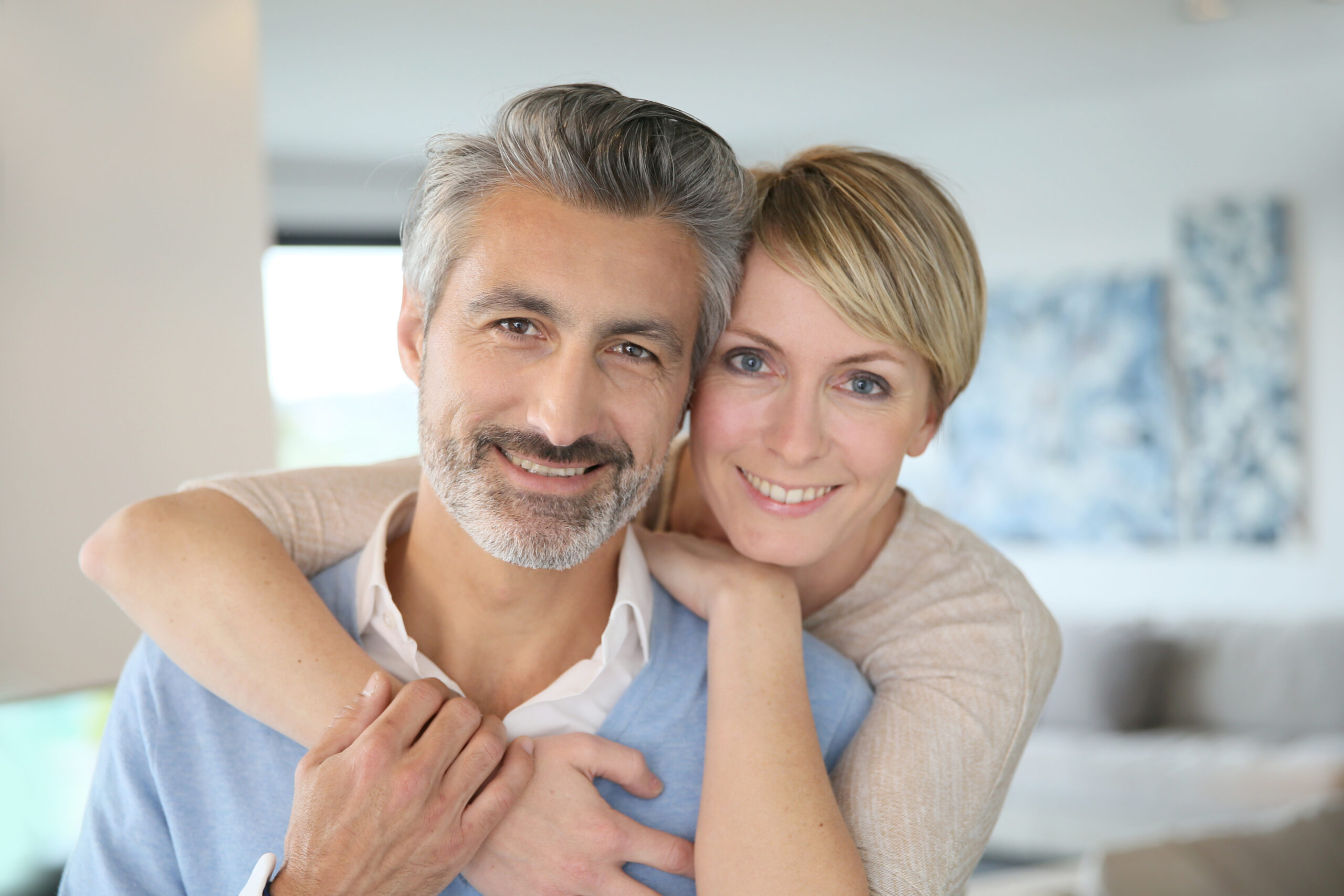 Smiling middle-aged couple standing in brand new home Middle aged couple who care for each other; man has prostate cancer and needs life insurance. They have found a solution.