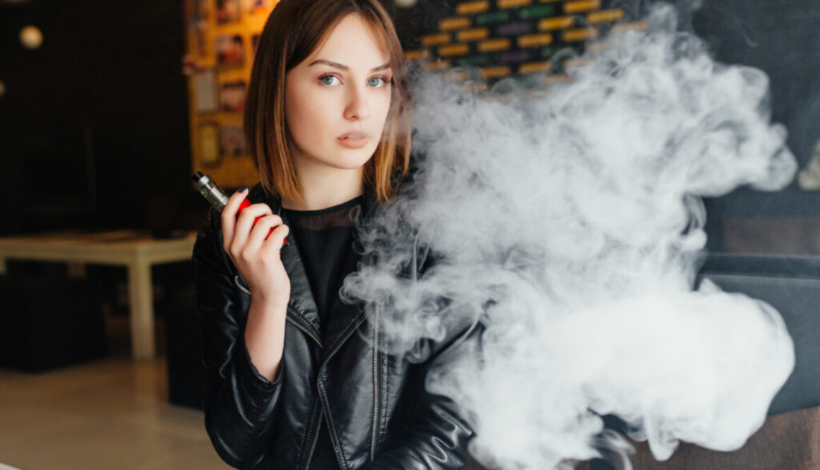 An attractive woman is vaping with a smile because she learned about Underwriting Exceptions for Tobacco Users Vaper Kayla
