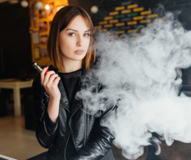 An attractive woman is vaping with a smile because she learned about Underwriting Exceptions for Tobacco Users